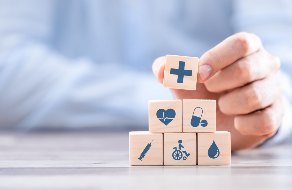 A person holds wooden blocks featuring various medical icons, symbolizing health insurance and wellness concepts. Get covered.